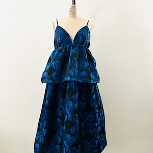 May include: A two-piece formal dress with a deep V-neckline and spaghetti straps. The dress features a blue floral pattern on a black background. The top has a peplum design, and the skirt is a midi length.