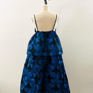 May include: A formal dress with a blue floral pattern on a black background. The dress features a layered design with spaghetti straps. The garment is displayed on a mannequin against a white backdrop.