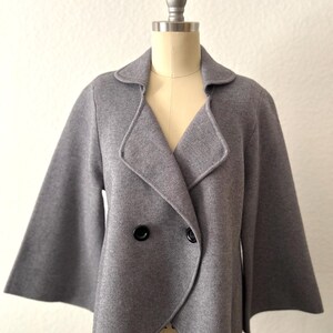 May include: A gray double-breasted knitted jacket with long, wide sleeves and a curved hem.