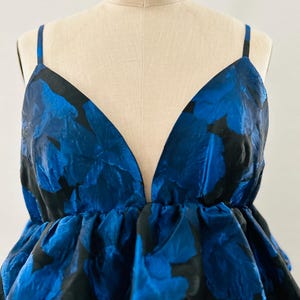 May include: A sleeveless top with a deep V-neck and a floral pattern in shades of blue and black. The top is displayed on a mannequin with the text "ROYAL FORM" at the top. The fabric has a textured appearance.