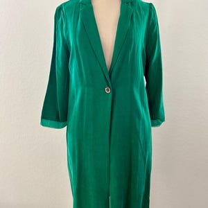 May include: A long, emerald green blazer with a single button closure. The blazer has a classic lapel and three-quarter length sleeves. The garment is displayed on a mannequin.