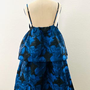 May include: A two-piece formal dress with a black base and a vibrant blue floral pattern. The top features thin straps and a layered design, while the skirt flows down. The dress is displayed on a mannequin.