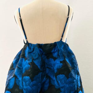 May include: A blue and black floral print dress on a mannequin. The dress features a layered skirt and thin black straps. The floral pattern is a vibrant blue against a black background, creating a striking contrast. The dress is designed for a formal occasion.