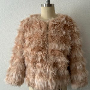 May include: A soft, pink faux fur jacket with a cropped length and long sleeves. The jacket is displayed on a mannequin.