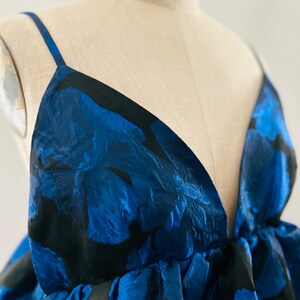 May include: A sleeveless dress with a deep V-neckline. The fabric features a bold floral pattern in shades of blue and black. The dress is displayed on a mannequin, showcasing its design and fit. The dress has thin straps.