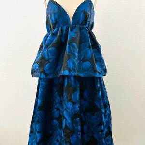 May include: A two-piece formal dress with a deep V-neckline and spaghetti straps. The dress features a black background with a vibrant blue floral pattern. The top has a peplum design, and the skirt is a midi length.