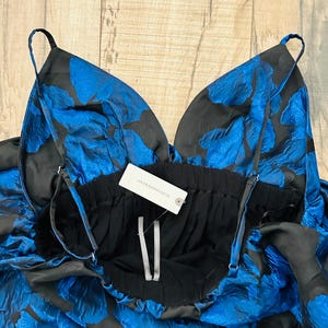 May include: A black and blue floral print dress with thin straps. The dress features a deep V-neckline and a gathered waist. The fabric has a textured appearance. A tag that says "Anthropologie" is attached to the dress.