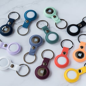 May include: Assortment of colorful silicone keychains with a silver ring and a small Apple logo in the center. The keychains are in various colors, including blue, green, purple, white, orange, yellow, and red.