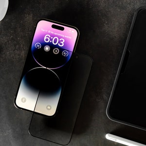 May include: A gold iPhone with a black screen protector. The phone's screen displays the time 6:03 and the date Tue 11. The phone is sitting on a dark gray surface.