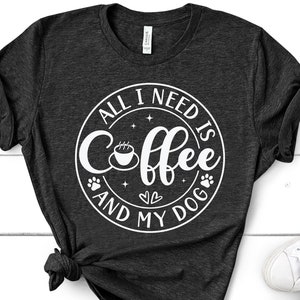 May include: A dark grey t-shirt with a white circle design that says "All I need is coffee and my dog". The design includes a coffee cup, paw prints, and hearts.