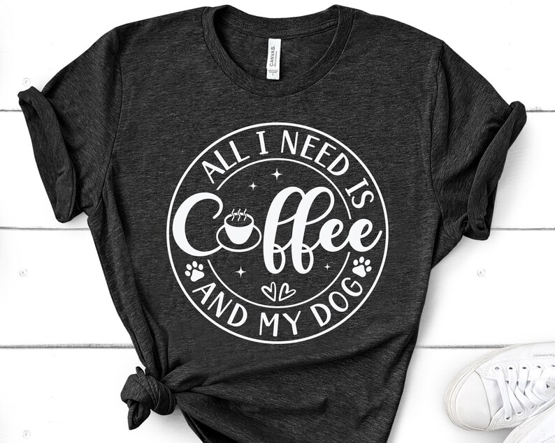 May include: A dark grey t-shirt with a white circle design that says "All I need is coffee and my dog". The design includes a coffee cup, paw prints, and hearts.