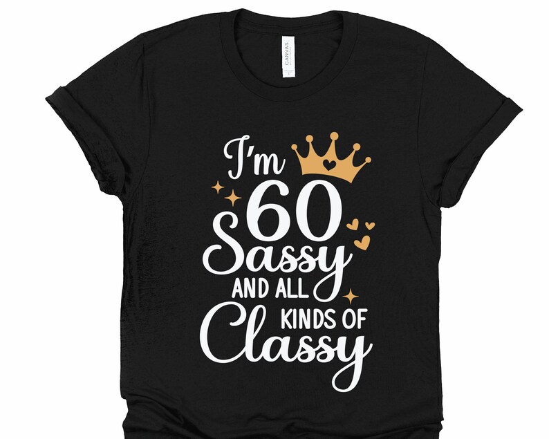 以下が含まれることがあります： 黒いTシャツに白い文字で「I'm 60 Sassy and all kinds of Classy」と書かれています。文字は金の王冠とハートで飾られています。