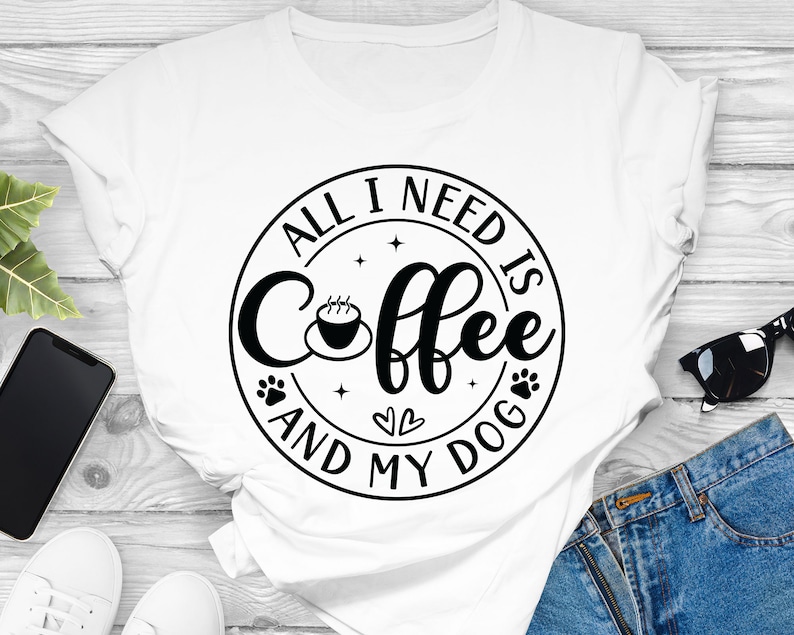 May include: White t-shirt with a black circle graphic that says "All I need is coffee and my dog" with a coffee cup, paw prints, and hearts.