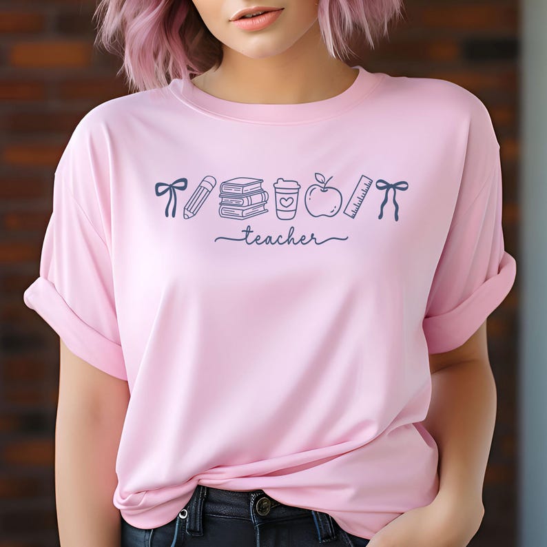 May include: A light pink t-shirt with rolled-up sleeves. The shirt features a dark blue graphic of school-related items, including a pencil, books, a coffee cup, an apple, and a ruler. The word "teacher" is written in cursive below the graphics.