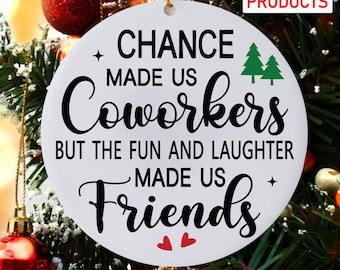 Op de afbeelding: Ronde witte ornament met zwarte tekst die luidt: "Toeval heeft ons collega's gemaakt, maar het plezier en het lachen hebben ons vrienden gemaakt". Er zijn twee kleine rode hartjes aan de onderkant van de ornament.