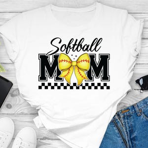 May include: White t-shirt with black text that reads "Softball Mom" with a yellow softball bow in the middle of the text.