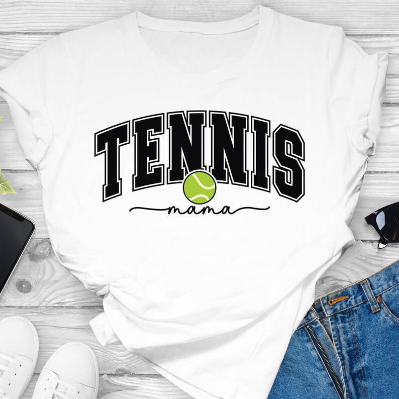 Może przedstawiać: Biała koszulka z czarnym napisem "Tennis mama" i zielonym obrazkiem piłki tenisowej.
