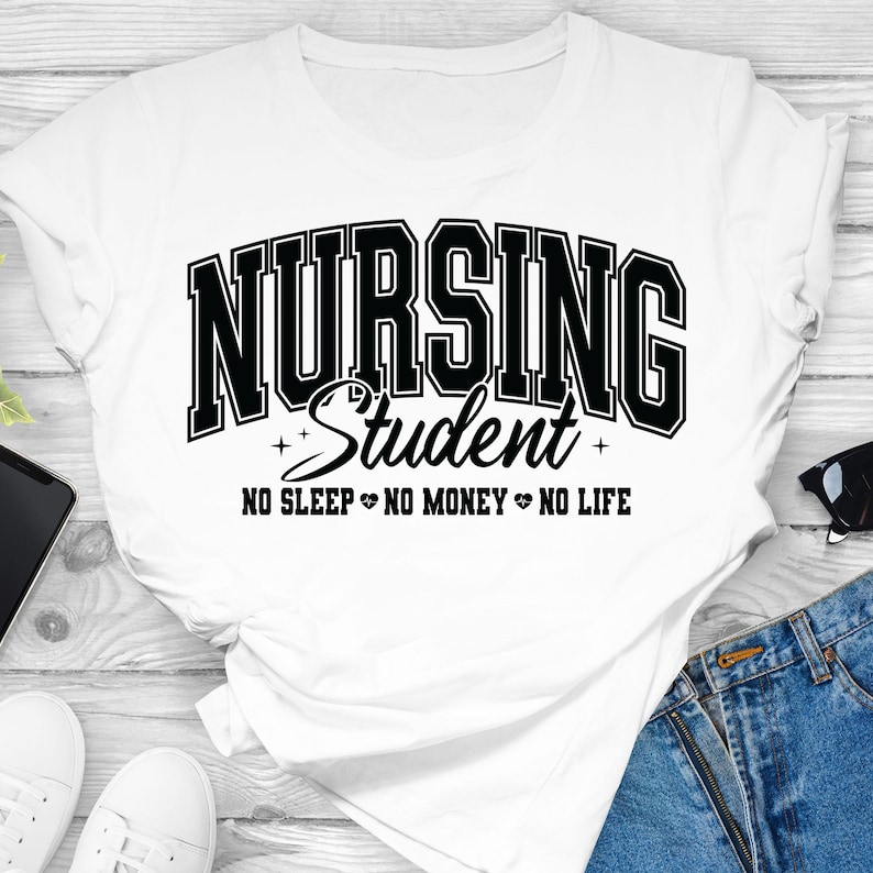 Op de afbeelding: Wit T-shirt met de tekst "NURSING Student" in een zwarte, collegiale lettertype. Daaronder staat de zin "NO SLEEP NO MONEY NO LIFE" in een zwart, schreefloos lettertype. Het shirt ligt op een witte ondergrond.