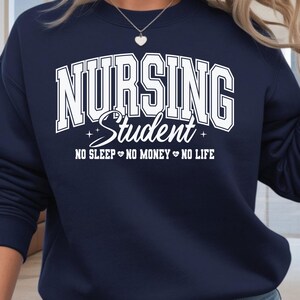 Op de afbeelding: Marineblauwe sweatshirt met de witte tekst "NURSING Student". Daaronder staat de zin "NO SLEEP NO MONEY NO LIFE". De sweatshirt heeft een ronde hals.