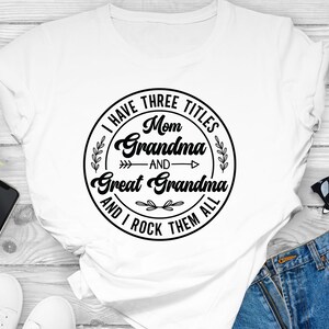 May include: White t-shirt with a black circle graphic that says "I have three titles: Mom, Grandma, and Great Grandma and I rock them all".