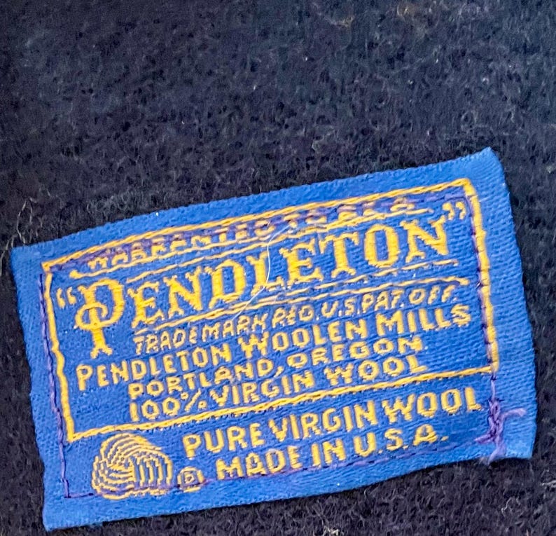 May include: A blue and yellow Pendleton label with the text "PENDLETON" and "TRADEMARK REG. U.S. PAT. OFF." The label also states "100% VIRGIN WOOL" and "MADE IN U.S.A."