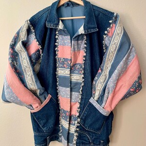 May include: A blue denim jacket with patchwork sleeves and front panels. The sleeves feature pink polka dots, floral patterns, and lace trim. The front panels alternate between pink, blue, and floral fabrics. The jacket has a classic collar and pockets.