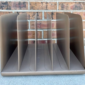 May include: A metal file organizer with six compartments. The organizer is a light brown color and has a smooth, slightly curved surface.