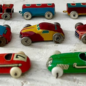 May include: A collection of vintage toy cars, including a red and blue car, a yellow and red car, a red car with a number 7, a green car with a number 5, a red and blue train, and a red and blue car. The cars are made of metal and have a worn, vintage look.