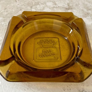 May include: Amber glass ashtray with a square shape and a raised design of a crown and the words "Best Western" in the center.