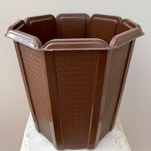 May include: A brown, octagonal plastic planter with a textured surface. The planter has a wide opening and a slightly flared shape. The design is simple and functional, suitable for various plants and flowers.
