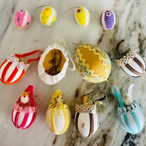 May include: Assortment of handmade Easter eggs in various colors and patterns, including white, yellow, pink, blue, and brown. Some eggs are decorated with lace and ribbons, while others have a more simple design. The eggs are perfect for decorating a home for the Easter holiday.