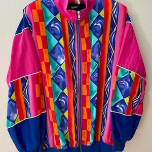 May include: A vibrant, vintage zip-up jacket featuring a bold geometric pattern in shades of pink, blue, orange, and green. The jacket has a high collar, elastic cuffs, and a blue bottom hem. The design includes vertical stripes and diamond shapes.