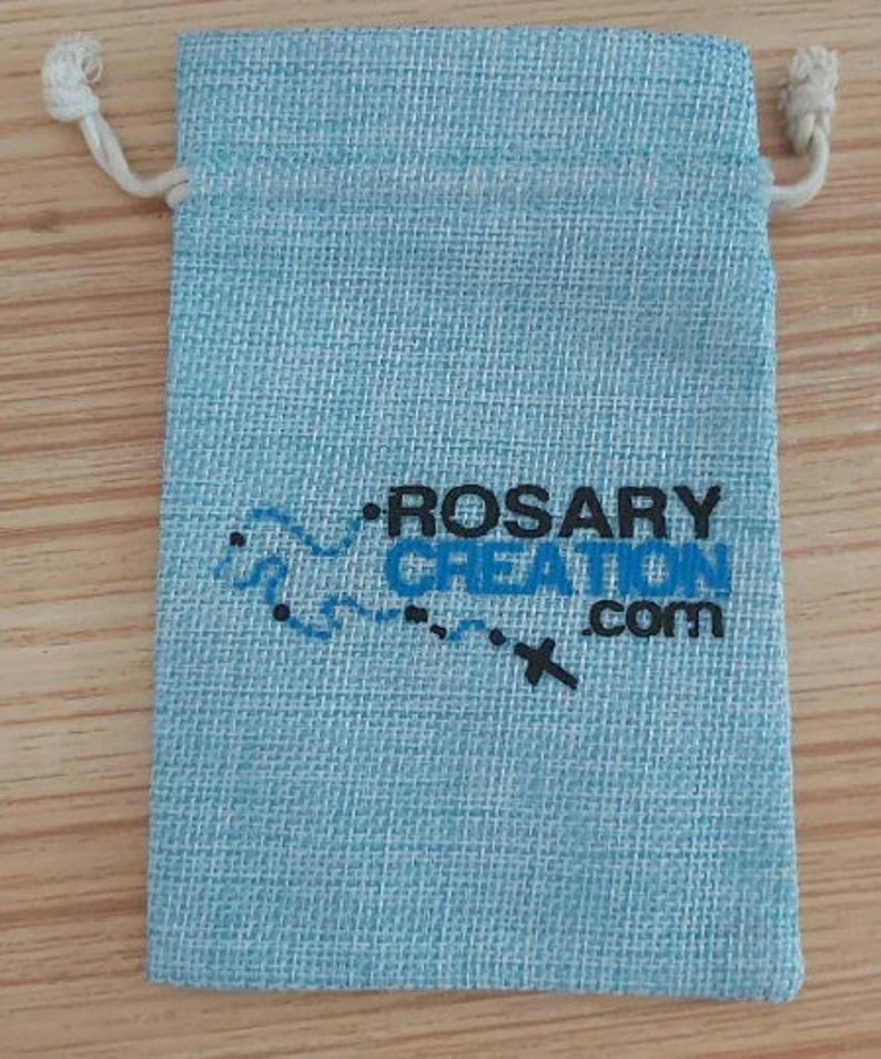 K&ouml;nnte beinhalten: Hellblaues Beutel mit Kordelzug und dem Text "ROSARY CREATION .com" in Schwarz und Blau. Der Beutel hat eine strukturierte Oberfl&auml;che und einen wei&szlig;en Kordelverschluss.