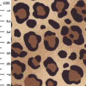 May include: Close-up of a tan fabric with a leopard print pattern. The pattern features dark brown and light brown spots. The image includes a ruler with centimeter measurements.