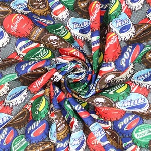Può includere: Un motivo di tessuto colorato con un design ripetitivo di tappi di bottiglia con vari nomi di marchi e slogan, tra cui "Rebel Blood", "Thirsty", "Pop", "Soda" e "Milk".