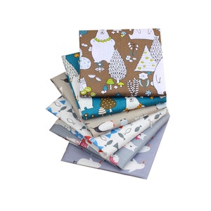 May include: A stack of fabric squares with various patterns. The top square features white bears, trees, and mushrooms on a brown background. Other squares display fish, penguins, and other designs in blue, gray, and white.
