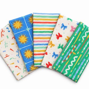 May include: Five folded fabric swatches arranged in a fan shape. The patterns include cream with colourful confetti, blue with yellow stars, multicoloured horizontal stripes, cream with small bows, and green with candles and wavy lines.
