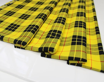 Op de afbeelding: Gele, zwarte en rode tartan stof gevouwen in drieën. De stof heeft een traditioneel ruitpatroon.