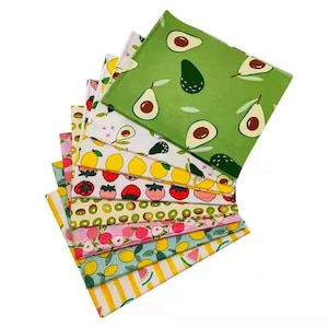 May include: A stack of ten fabric squares with different fruit patterns. The top square is green with avocado illustrations. The other squares feature lemons, strawberries, kiwi, peaches, and watermelon.