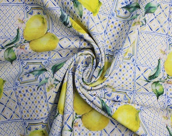 Puede incluir: Tela con un patrón repetido de limones amarillos, hojas verdes y flores blancas sobre un fondo blanco y azul similar a azulejos. La tela está drapeada, mostrando la continuidad del patrón.