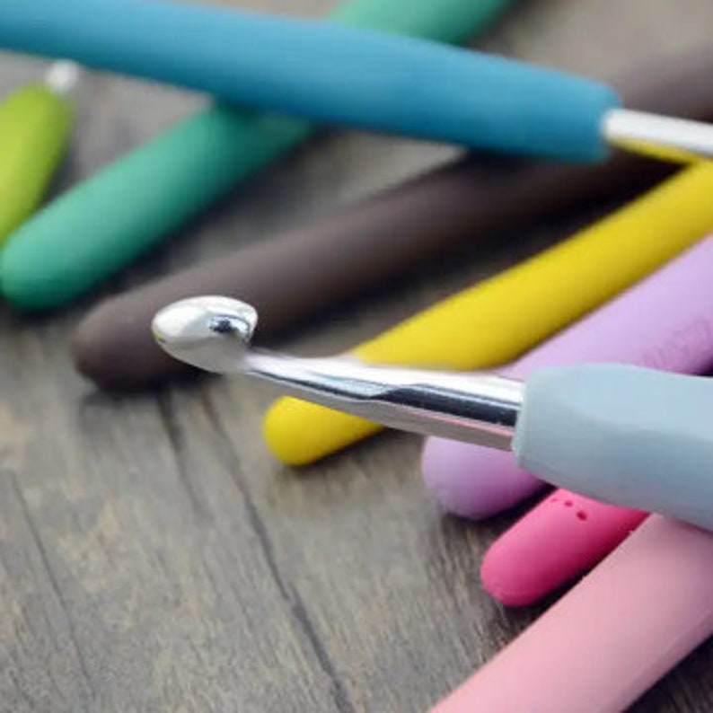 May include: A close-up of a set of colorful crochet hooks with silver tips. The hooks are arranged in a pile on a wooden surface.