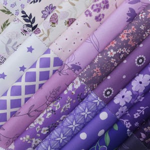 May include: A collection of rolled fabric in various shades of purple, lavender, and white. The fabrics feature floral, geometric, and star patterns. Some rolls have small pink flower accents. The fabrics are arranged diagonally, showcasing the variety of designs.