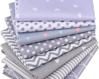 May include: A stack of eight fabric squares with different patterns. The top square is light purple with white hearts, the next is gray with white polka dots, the next is gray with white triangles, the next is gray with white polka dots, the next is gray with a chevron pattern, the next is gray with white stripes, the next is gray with a geometric pattern, and the bottom square is gray with a geometric pattern.