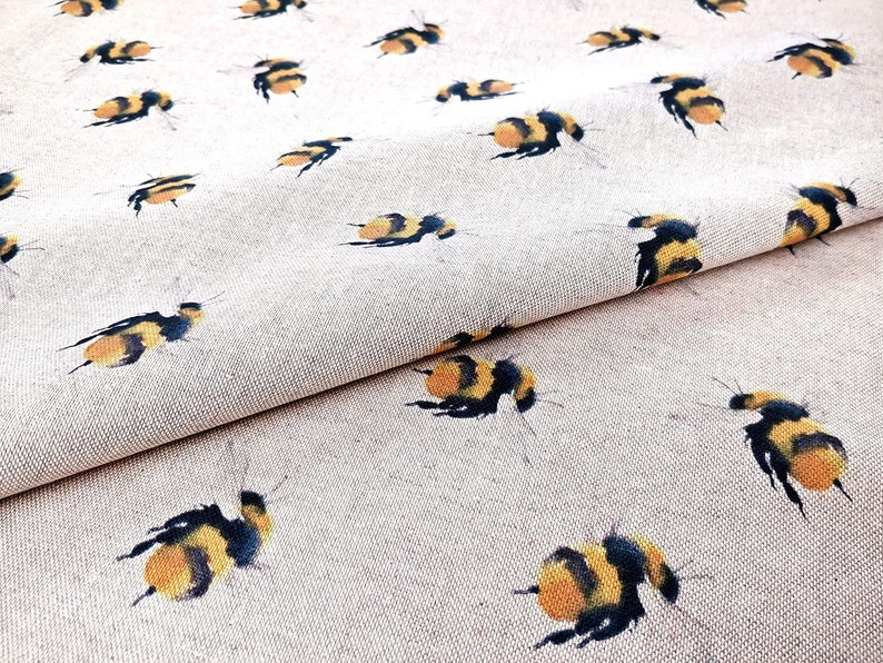 May include: A beige fabric with a repeating pattern of yellow and black bumblebees. The fabric is folded in half, showing the pattern on both sides.