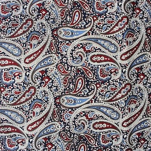 Puede incluir: Primer plano de una tela con estampado de cachemira. El diseño presenta grandes motivos en forma de lágrima en tonos rojos, azules y blancos sobre un fondo azul marino oscuro. El intrincado patrón se repite en toda la tela.