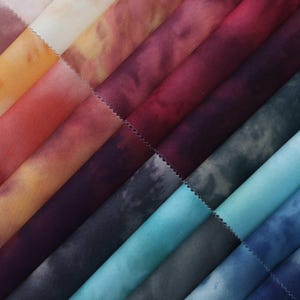 May include: A selection of fabric swatches in a diagonal arrangement, showcasing a spectrum of colours. The swatches feature shades of orange, red, purple, teal, and blue. Each fabric piece has a textured look and a zigzag edge.