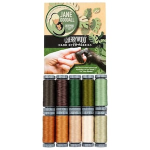 May include: A collection of ten spools of Aurifil cotton thread arranged in two rows, featuring earthy tones including brown, green, tan, and beige. Above the thread is a Cherrywood Hand Dyed Fabrics card featuring Jane Goodall.