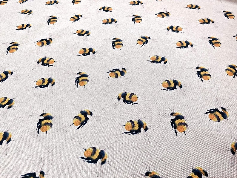 May include: A beige fabric with a repeating pattern of black and yellow bumblebees. The bumblebees are stylized and have a watercolor effect.