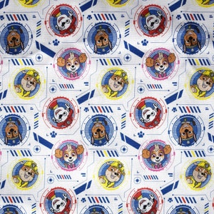 May include: White fabric with a repeating pattern of cartoon dogs in various poses. The dogs are wearing different colored uniforms and are surrounded by blue and red geometric shapes.