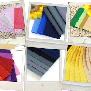 Op de afbeelding: Assortiment van stofstalen in verschillende kleuren, waaronder roze, rood, blauw, grijs, paars, geel en beige. De stalen zijn in een waaier vorm gerangschikt en worden weergegeven op een witte achtergrond.